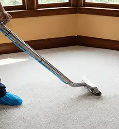 Steam carpet cleaning technician using a hot-water extraction wand on a residential carpet, wearing blue protective shoe covers Reno, NV.