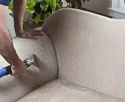 Professional upholstery cleaner deep-cleaning a fabric sofa with a handheld extraction tool and hose in Reno, NV.